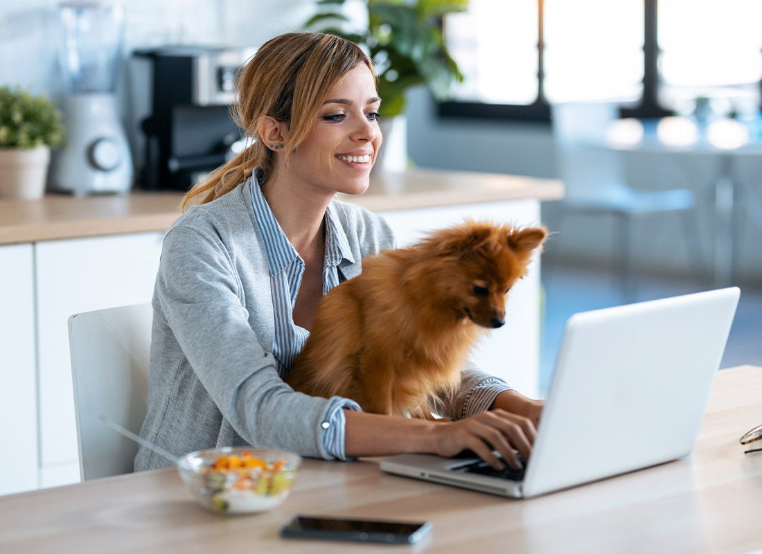 Read Our Reviews - Cute Little Dog Looking at a Laptop While Her Owner Works With Him in the Kitchen at Home